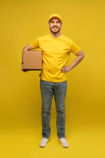 Portrait of excited delivery man in yellow uniform holding paper box isolated over yellow background. — Stock Photo, Image