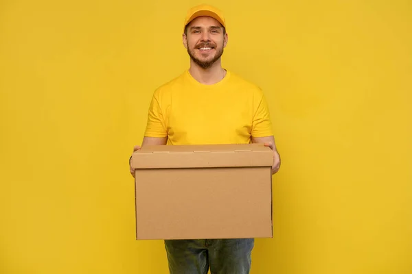 Retrato del repartidor excitado en caja de papel uniforme amarillo aislado sobre fondo amarillo . — Foto de Stock