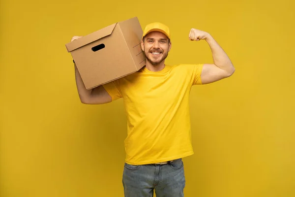 Portrait of excited delivery man in yellow uniform holding paper box isolated over yellow background. — Stock Photo, Image