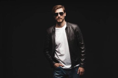 Moda adamı, yakışıklı erkek manken portresi güneş gözlüğü ve deri ceket, siyah arka planda genç bir adam..