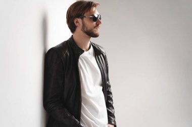 Moda adamı, yakışıklı erkek manken portresi güneş gözlüğü ve deri ceket, beyaz arka planda genç bir adam.
