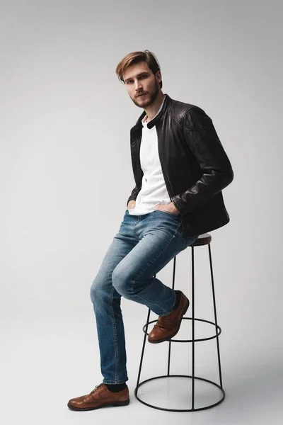 Fashion man, Handsome serious beauty male model portrait wear leather jacket, sitting on chair over white background. — Stock Photo, Image