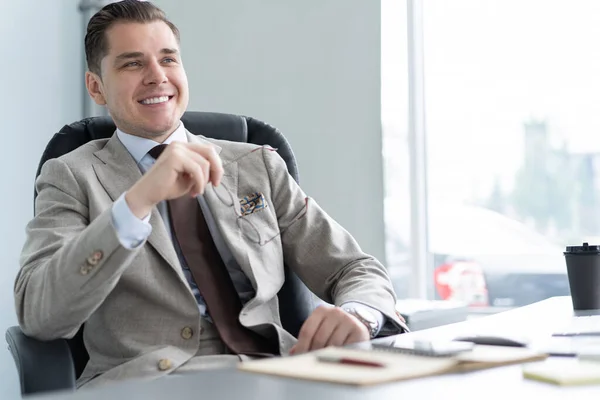Männliche Gelegenheitsarbeiterin lächelt im Büro, sitzt am Arbeitsplatz. — Stockfoto