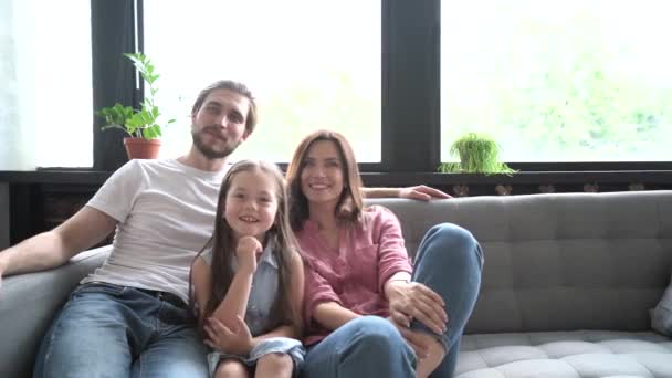 Šťastný rodinný portrét, mladí dospělí pěstouni matka a otec sbližování s legrační roztomilé děti smějící se pohled na fotoaparát pózovat společně na gauči v moderním domě — Stock video