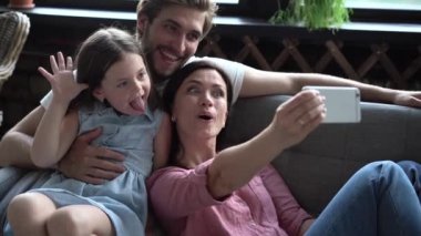 Mutlu bir aile kanepede oturuyor, gülümseyen bir anne cep telefonu tutuyor, selfie çekiyor. Kızıyla fotoğraf çektirmek için heyecanlı bir çift