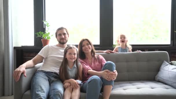 Glückliches Familienporträt, junge erwachsene Pflegeeltern Mutter und Vater Bindung mit lustigen niedlichen Kindern Kinder lachen Blick in die Kamera posiert zusammen auf der Couch in modernen Haus — Stockvideo