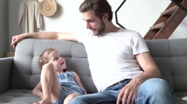 Mutlu aile, tatlı anaokulu kızı ve babası kanepede birlikte yatarak gülerek eğleniyorlar.