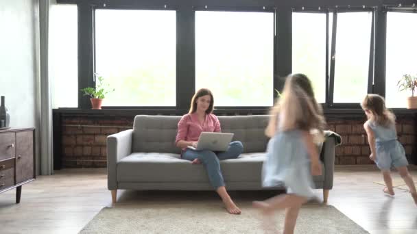 2人の騒々しい実行中の子供たちに気を取られて、ラップトップ上の自宅から働くために苦労して美しいストレスシングルマザー — ストック動画