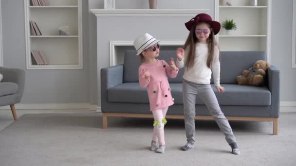 İki kız kardeş oturma odasında zıplayıp eğleniyor. Aktif ve neşeli kızlar evde dans ediyor. Birlikte boş zamanların tadını çıkarıyorlar. — Stok video