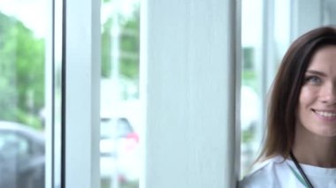 Beyaz sağlık önlüğü ve steteskop giyen mutlu genç Avrupalı kadın doktor kameraya bakıyor. Hastane ofisinde poz veren gülümseyen kadın doktor..