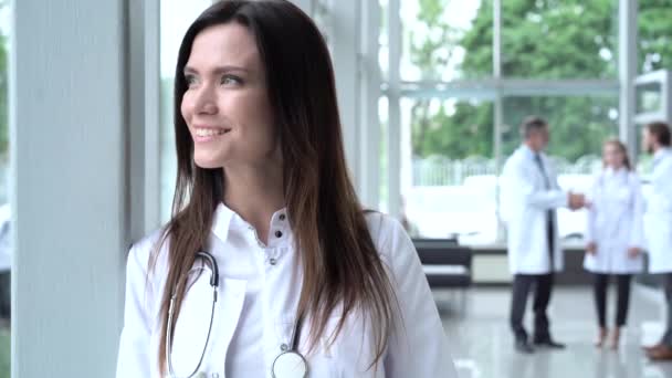 Jovem médica europeia feliz vestindo casaco médico branco e estetoscópio, olhando para a câmera. Médica sorridente posando no consultório do hospital . — Vídeo de Stock