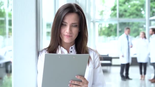 Dottoressa sorridente con una cartella in uniforme in piedi. Attraente medico in camice bianco e stetoscopio sorridente alla fotocamera in clinica — Video Stock