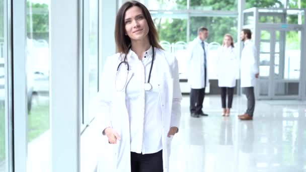 Jovem médica europeia feliz vestindo casaco médico branco e estetoscópio, olhando para a câmera. Médica sorridente posando no consultório do hospital . — Vídeo de Stock