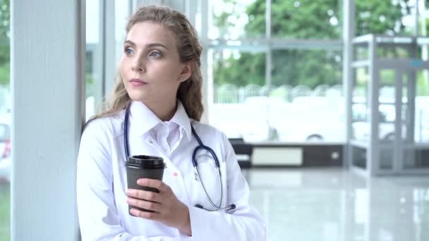 Όμορφη γυναίκα γιατρός στο γραφείο, παίρνει ένα διάλειμμα, πίνοντας καφέ και πολύ κουρασμένος κοιτάζοντας μέσα από το πανοραμικό παράθυρο. — Αρχείο Βίντεο