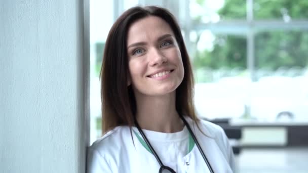 Een gelukkige jonge Europese arts met een witte jas en stethoscoop, kijkend naar de camera. Glimlachende vrouwelijke arts poseren in het ziekenhuis kantoor. — Stockvideo