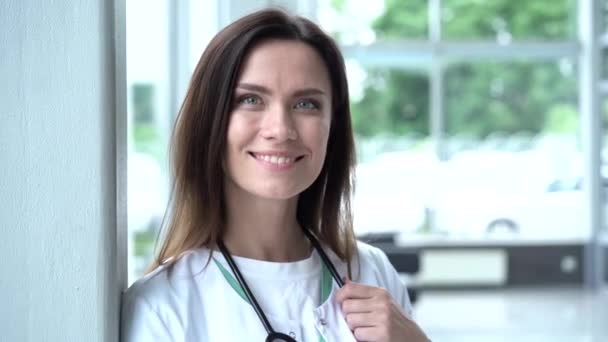 Feliz joven doctora europea vistiendo bata médica blanca y estetoscopio, mirando a la cámara. Médico sonriente posando en la oficina del hospital . — Vídeos de Stock