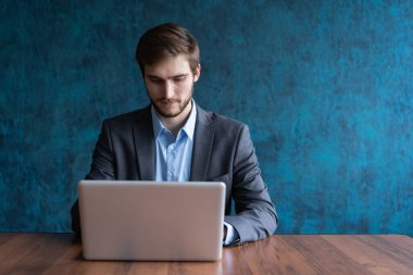 Ofis masasında dizüstü bilgisayar kullanan mutlu genç bir iş adamı..