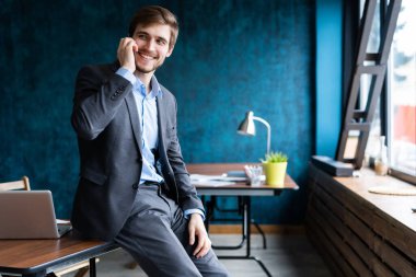 Takım elbiseli yakışıklı iş adamı ayakta duruyor ve akıllı telefonla konuşuyor.