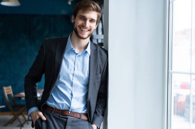 Ofisinin penceresinin yanında duran kendine güvenen profesyonel yakışıklı iş adamı.