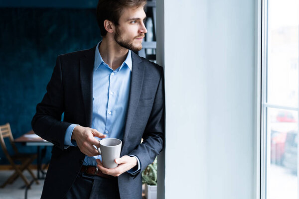 Happy attracive young businessman drinking coffee in office.