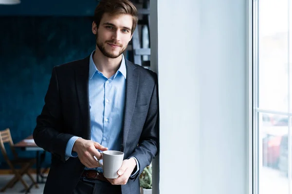 Szczęśliwy atrakcyjny młody biznesmen pijący kawę w biurze. — Zdjęcie stockowe