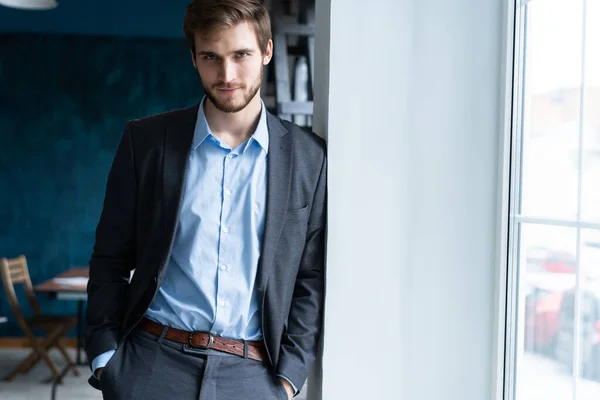 Selbstbewusster, gut aussehender Geschäftsmann steht am Fenster in seinem Büro — Stockfoto