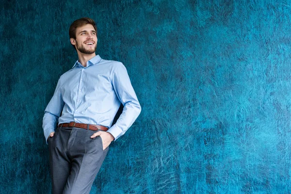 Portrait de beau jeune homme debout contre un mur bleu avec espace de copie. — Photo