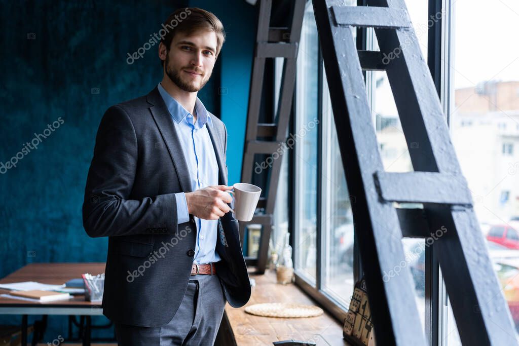 Happy attracive young businessman drinking coffee in office.