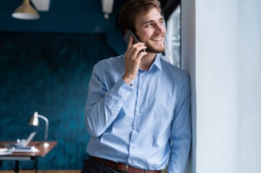 Takım elbiseli yakışıklı iş adamı ayakta duruyor ve akıllı telefonla konuşuyor.