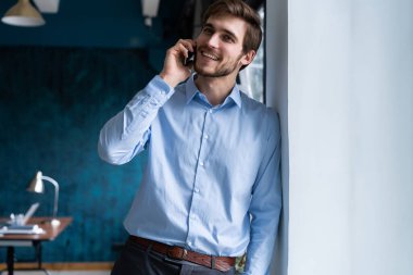 Takım elbiseli yakışıklı iş adamı ayakta duruyor ve akıllı telefonla konuşuyor.