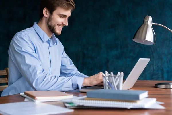 Pengusaha muda yang bahagia menggunakan laptop di meja kantornya. — Stok Foto
