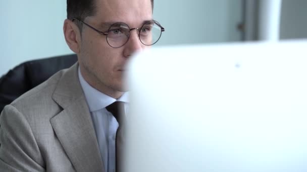 Случайный бизнесмен работает в офисе, сидит за столом, печатает на клавиатуре, смотрит на экран компьютера — стоковое видео