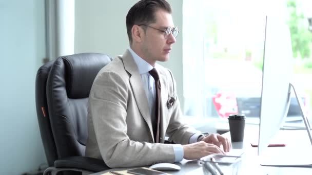 Случайный бизнесмен работает в офисе, сидит за столом, печатает на клавиатуре, смотрит на экран компьютера — стоковое видео