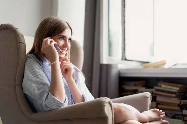 Young cheerful woman talking on mobile phone at home. — Stock Photo, Image