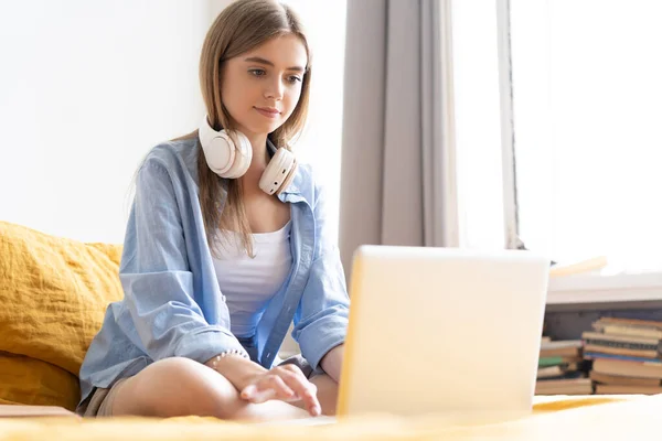 Pretty young student working at home on her laptop computer sitting on her bed. — Stock Photo, Image