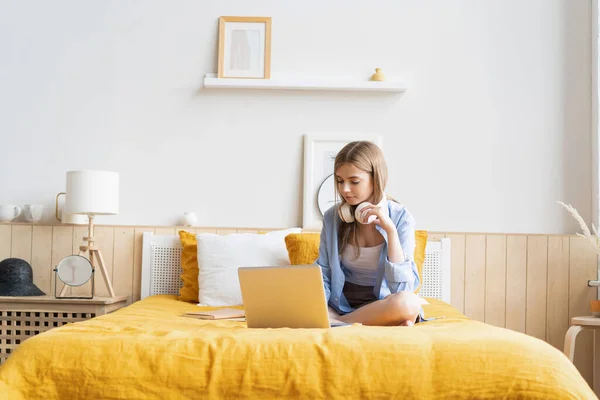 Pretty young student working at home on her laptop computer sitting on her bed. — Stock Photo, Image