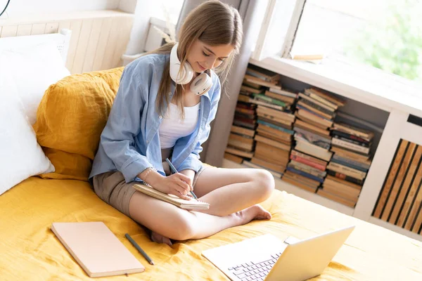 Όμορφη νεαρή φοιτήτρια που εργάζεται στο σπίτι στον φορητό υπολογιστή της κάθεται στο κρεβάτι της. — Φωτογραφία Αρχείου
