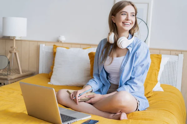 Όμορφη νεαρή φοιτήτρια που εργάζεται στο σπίτι στον φορητό υπολογιστή της κάθεται στο κρεβάτι της. — Φωτογραφία Αρχείου
