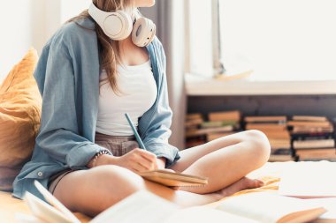 Çekici bir öğrenci kadın üniversiteden ödevlerini yazarken ve çalışırken yatağında uzanıyor.