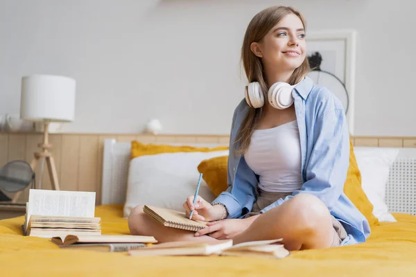 Attraktive Studentin liegt zu Hause auf ihrem Bett, während sie ihre Hausaufgaben vom College schreibt und bearbeitet — Stockfoto