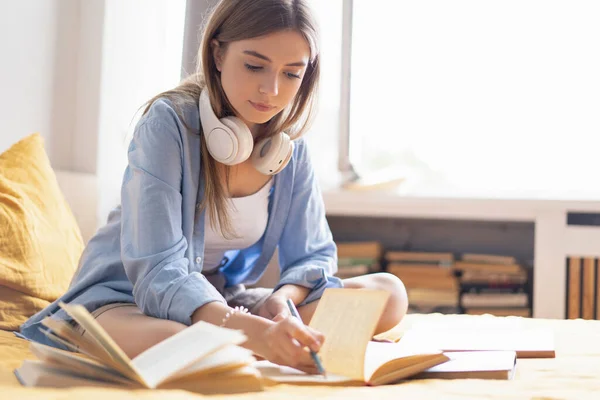 Attraktive Studentin liegt zu Hause auf ihrem Bett, während sie ihre Hausaufgaben vom College schreibt und bearbeitet — Stockfoto