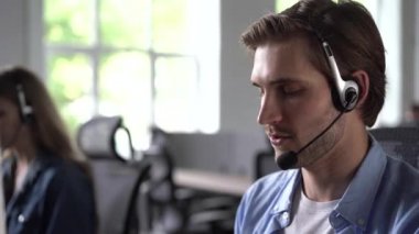 Odaklanmış erkek temsilci kulaklıklı çağrı merkezi ajanı ofiste bilgisayar kullanarak müşteriye şikayetlerde yardımcı oluyor