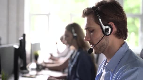 Agente de call center de representante masculino focado no fone de ouvido ajudando o cliente com reclamações usando o computador no escritório — Vídeo de Stock