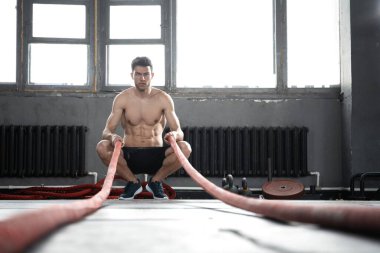 Savaş halatıyla atletik genç adam spor salonunda egzersiz yapıyor..