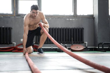 Savaş halatıyla atletik genç adam spor salonunda egzersiz yapıyor..