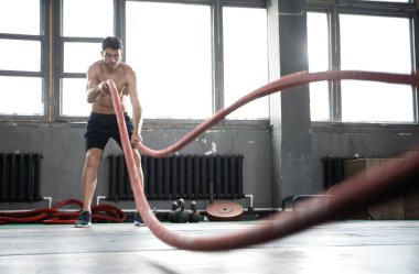 Savaş halatıyla atletik genç adam spor salonunda egzersiz yapıyor..