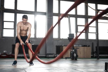 Savaş halatıyla atletik genç adam spor salonunda egzersiz yapıyor..