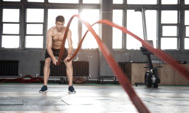 Savaş halatıyla atletik genç adam spor salonunda egzersiz yapıyor..