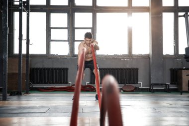 Savaş halatıyla atletik genç adam spor salonunda egzersiz yapıyor..