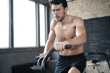 Spor salonunda egzersiz bisikleti kullanan bir adam. Spor salonunda spor yapan erkek, kardiyo çalışması için hava bisikleti kullanıyor.